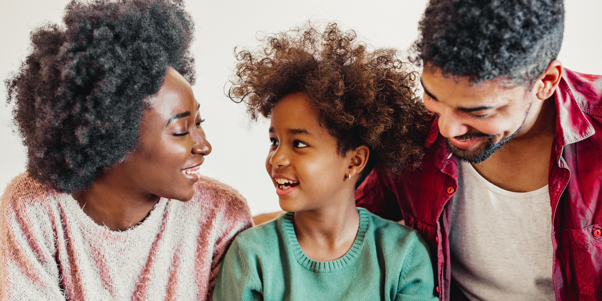 child sits between her mom and dad and they are talking and laughing