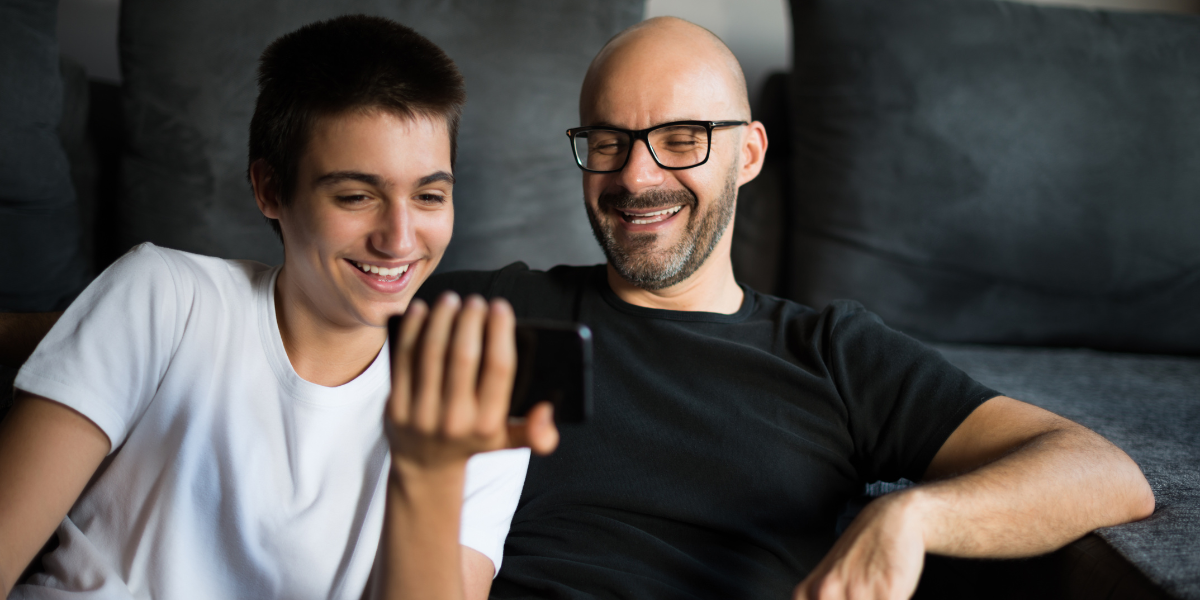 trans person sits with caregiver accessing virtual health on phone