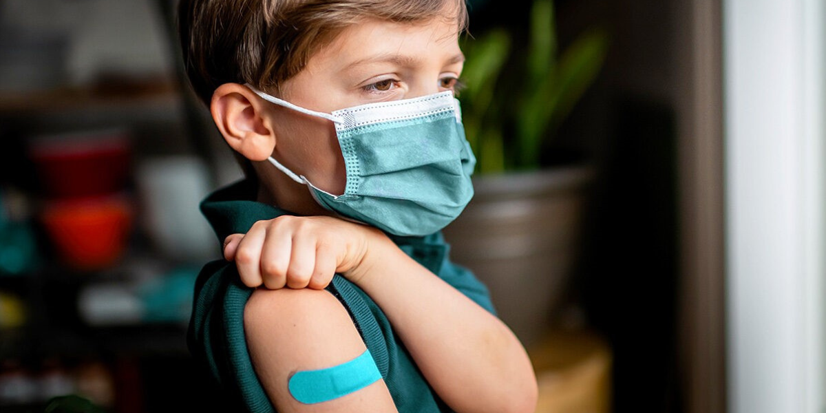A boy wearing a mask and a bandage on his upper arm